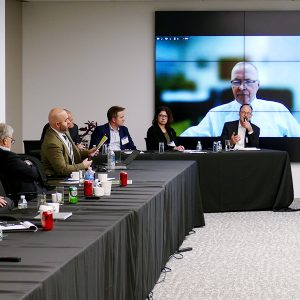 Audience members (on the left table) listen to panelists (beginning second from left) Walter Hopkins, 18th Square; Melissa Alfano, SEIA; Peter Fox-Penner, Boston University; and James Daly, Eversource (appearing virtually).