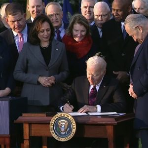 President Biden signs the bipartisan Infrastructure Investment and Jobs Act, surrounded by congressional leaders and supporters of the bill.